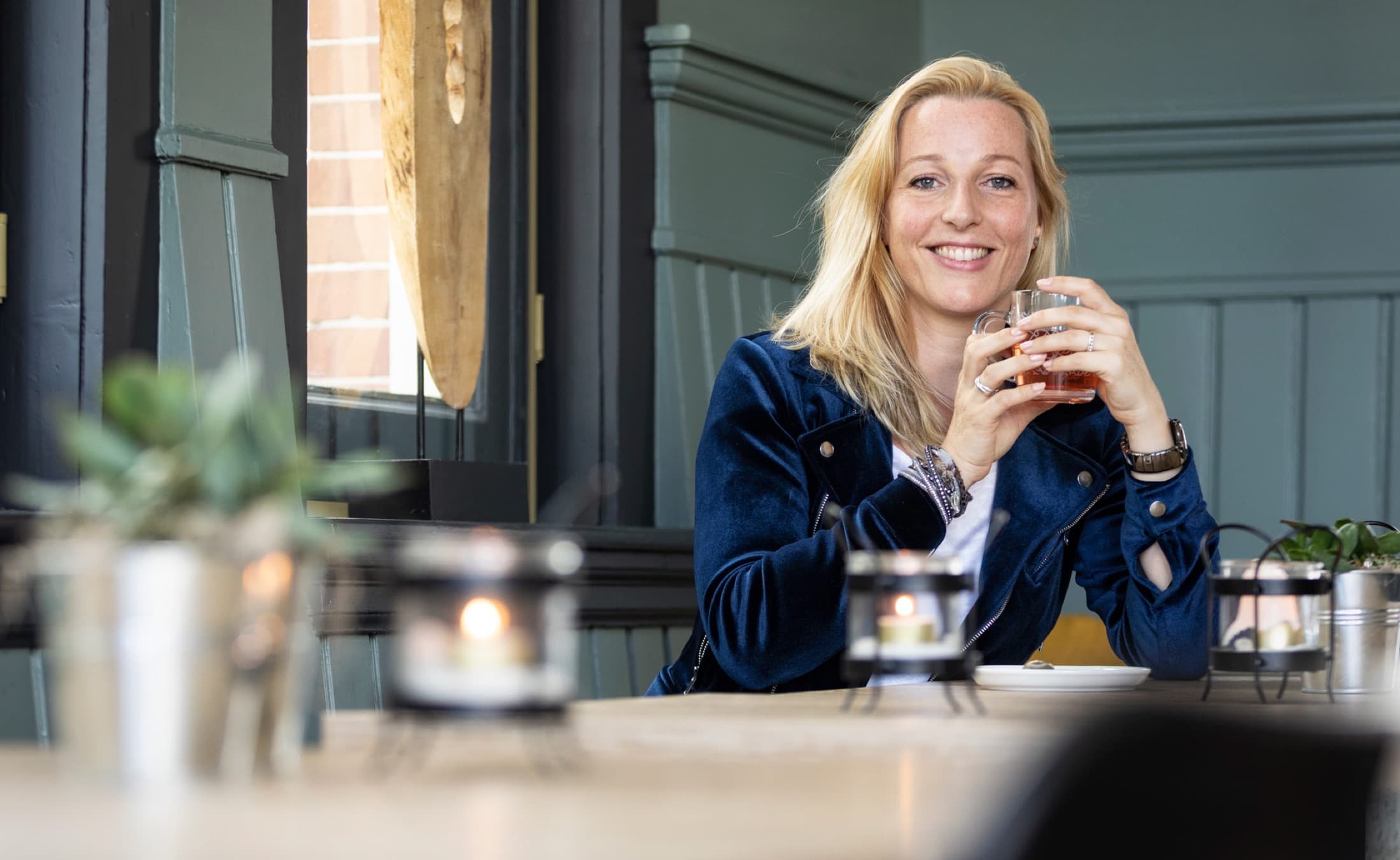 Laura Evers met een warme drank aan tafel in een sfeervolle ruimte