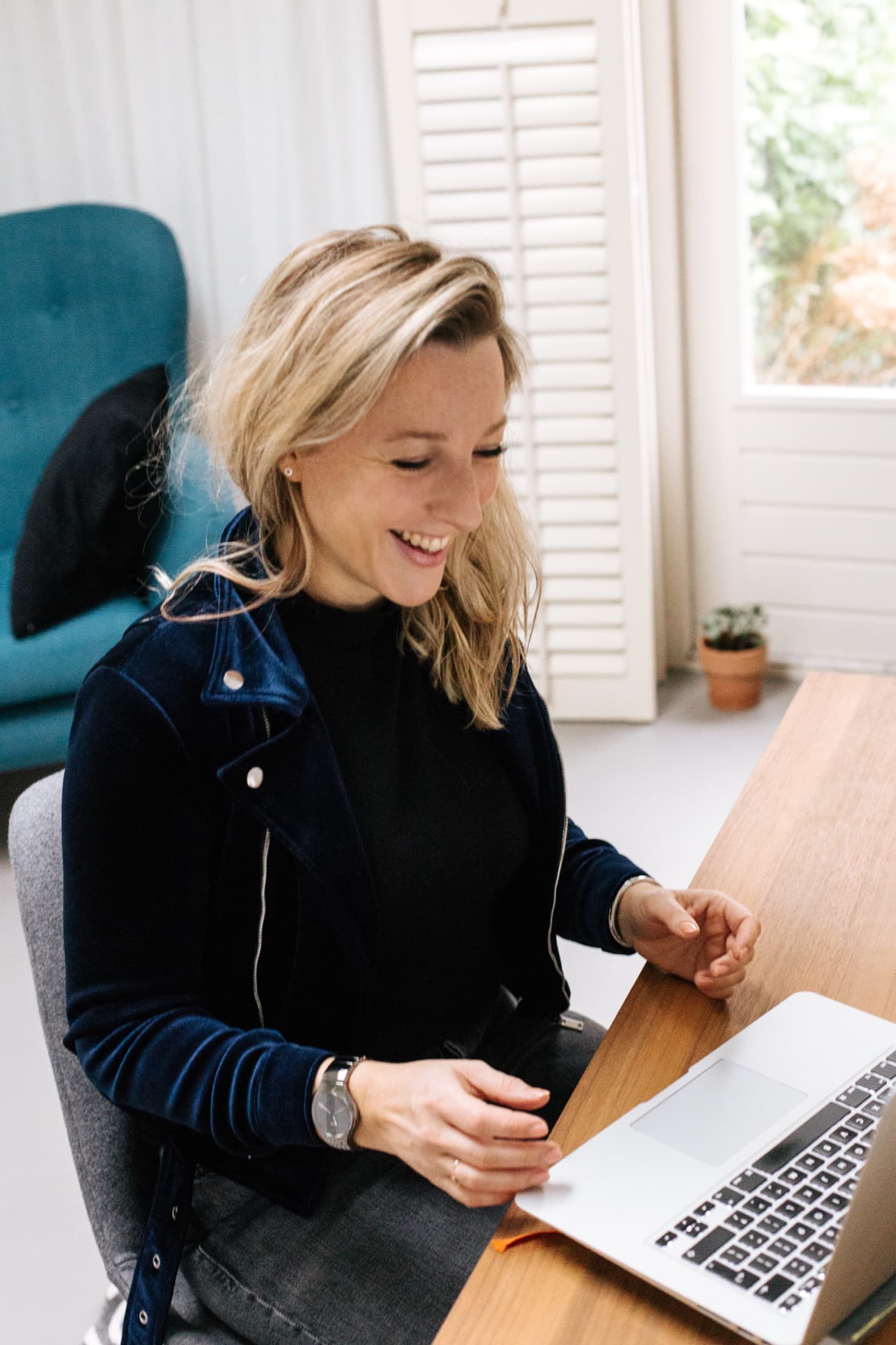 Laura Evers lachend achter haar laptop in een lichte werkruimte
